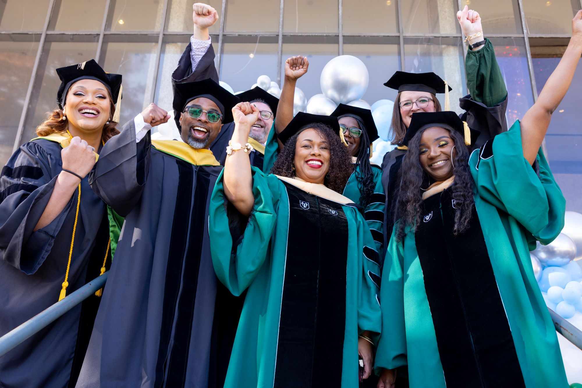 Robed students at graduation raising hands in the air.