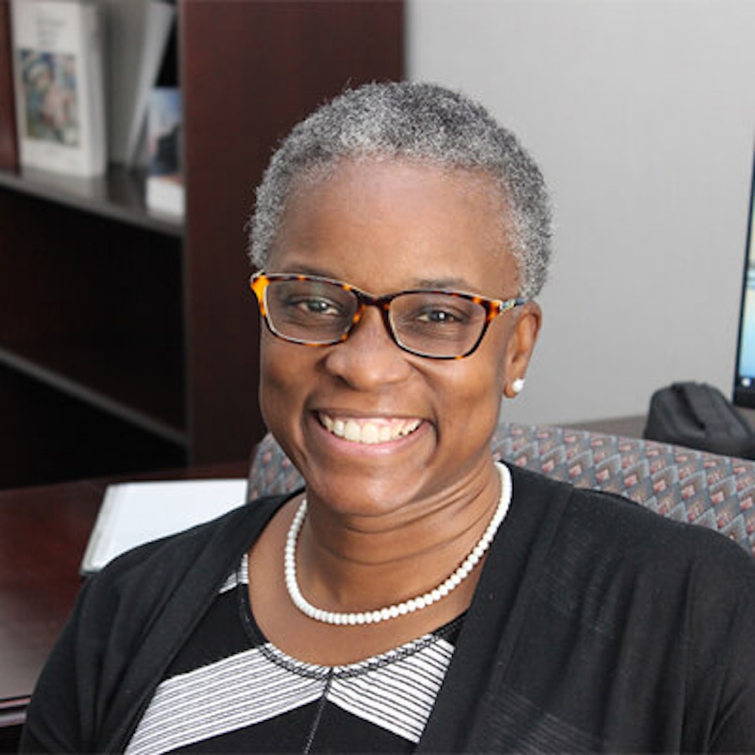 Smiling professional woman with gray hair, tortoise-shell glasses, in an office.