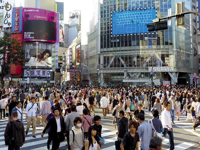 A large group of people walking in Tokyo, some masked, illustrating population epidemiology