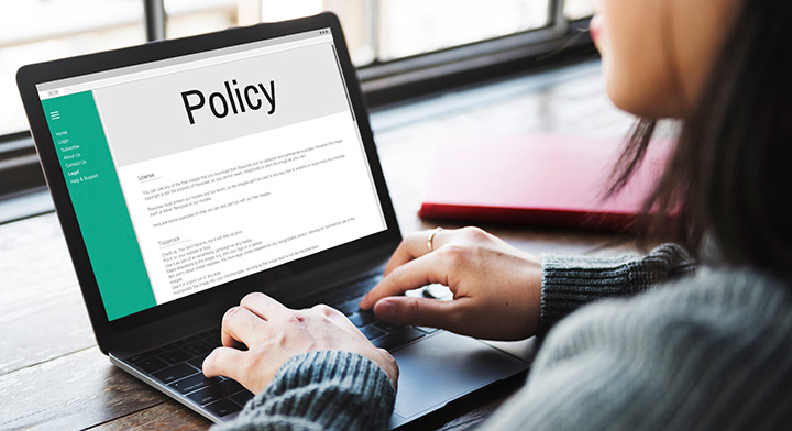 Woman on a laptop, where the screen shows the word "Policy."
